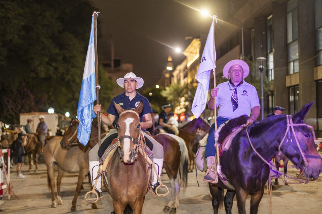 Dos cabalgantes, uno con la bandera Argentina y el otro con la bandera que lleva el logo de la asociación civil La Brocheriana.