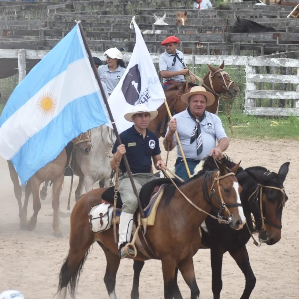 Dos cabalgantes ingresando a la Sociedad Rural de malagueño, uno con la bandera de Argentina y otro con la bandera que lleva el logo de La Brocheriana.